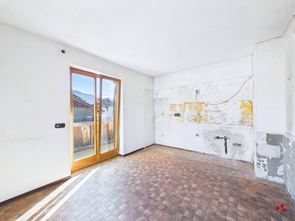 Ehemalige Küche mit Fliesenboden und Zugang zu einem Balkon, renovierungsbedürftig.