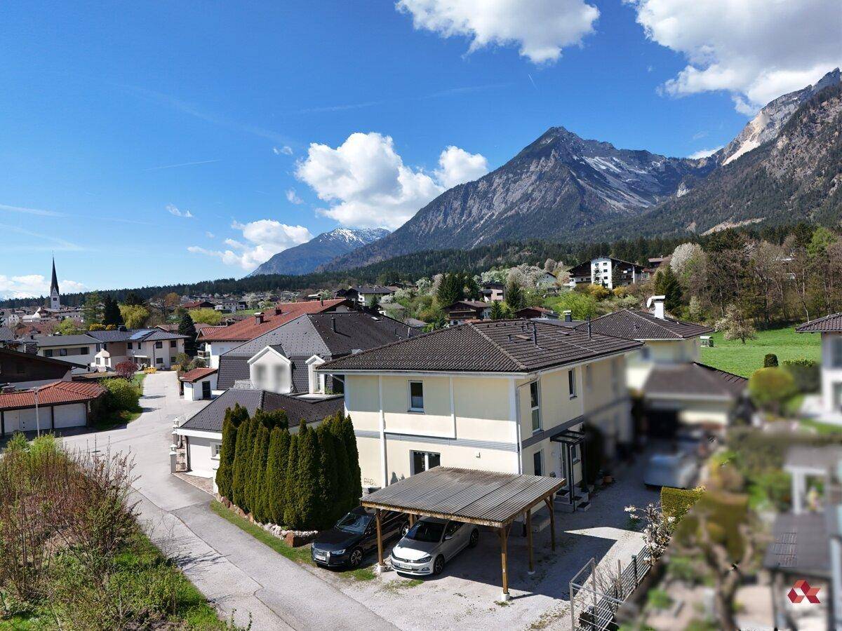 Luftaufnahme des Hauses mit Nachbarschaft und beeindruckendem Bergpanorama.