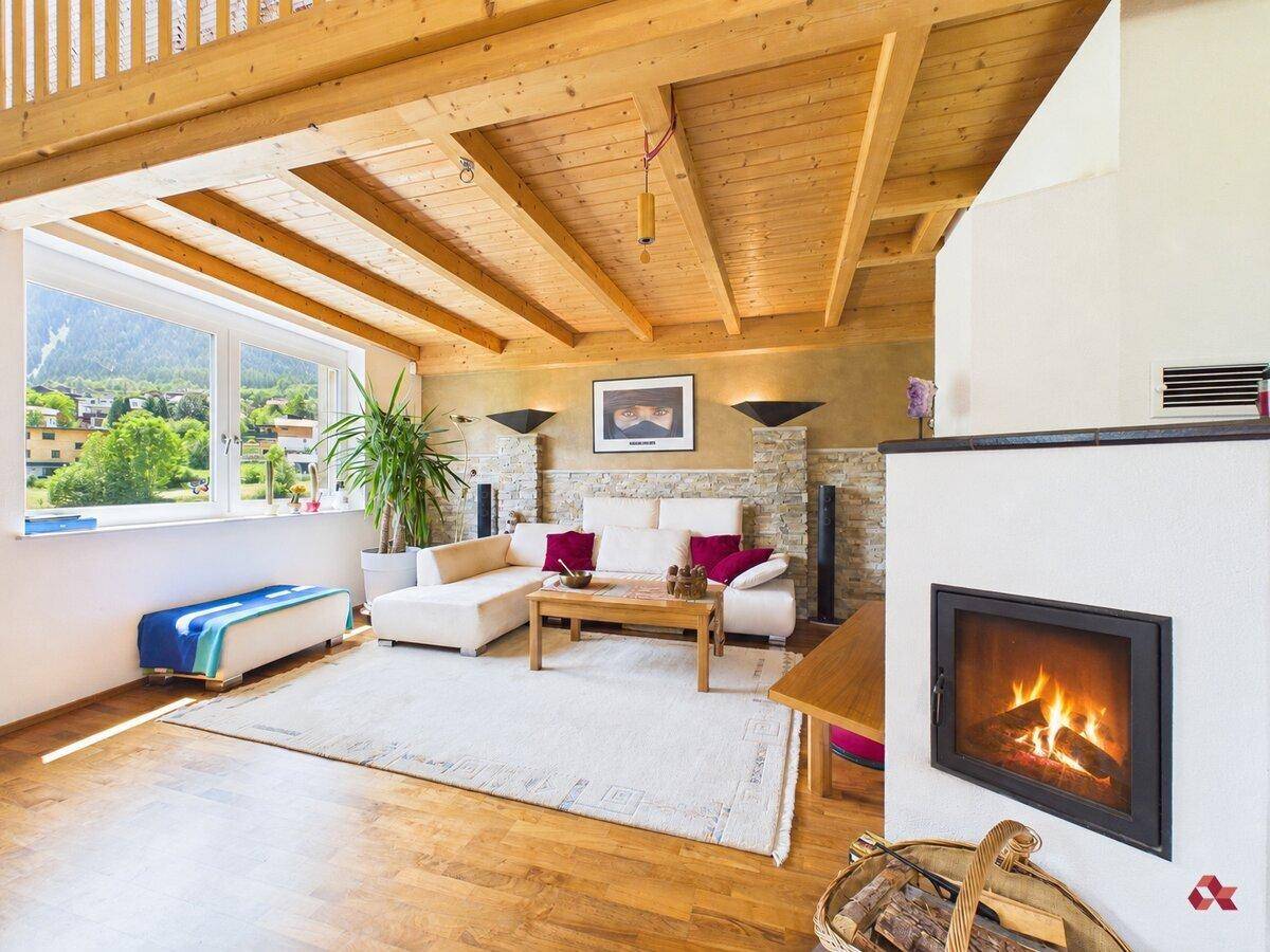 Gemütliches Wohnzimmer mit Kamin, Holzbalkendecke und großem Fenster mit Bergblick.