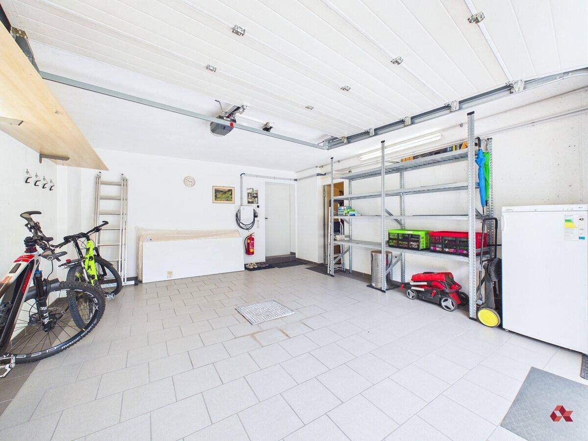 Geräumige Garage mit Fliesenboden, Regalen und Platz für Fahrräder und Fahrzeuge.