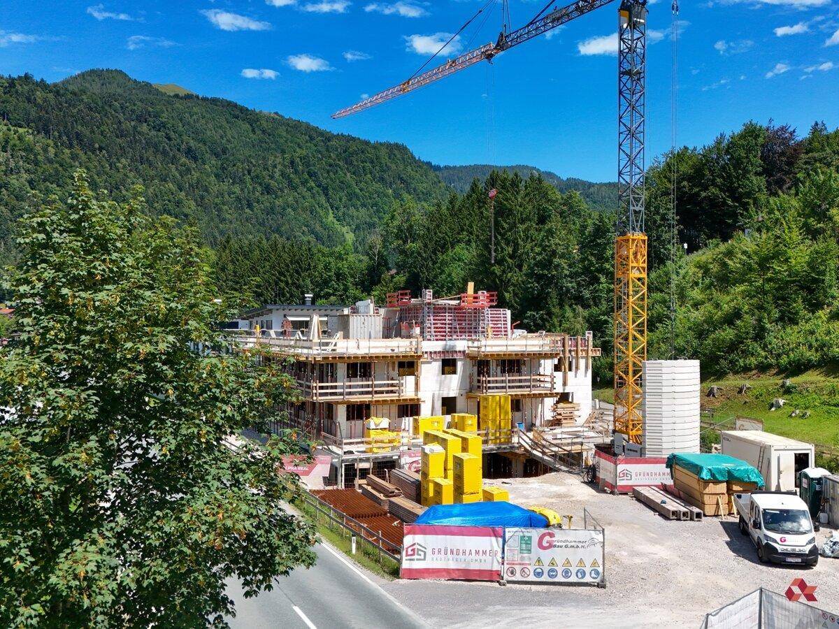 Baustelle eines Neubaus mit Kran vor einer malerischen Bergkulisse.
