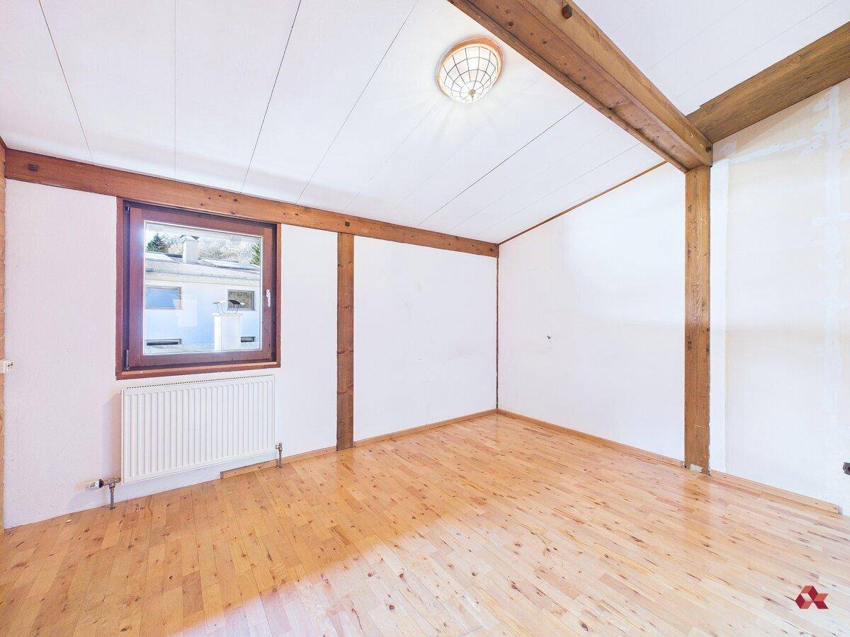Helles Schlafzimmer mit sichtbaren Holzbalken und Parkettboden, strahlt alpine Gemütlichkeit aus.