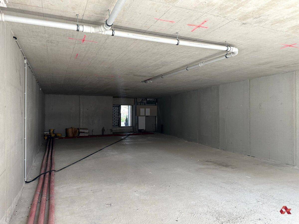 Unfertiger Gewerberaum im Rohbau mit Betonwänden und sichtbaren Installationen an der Decke.