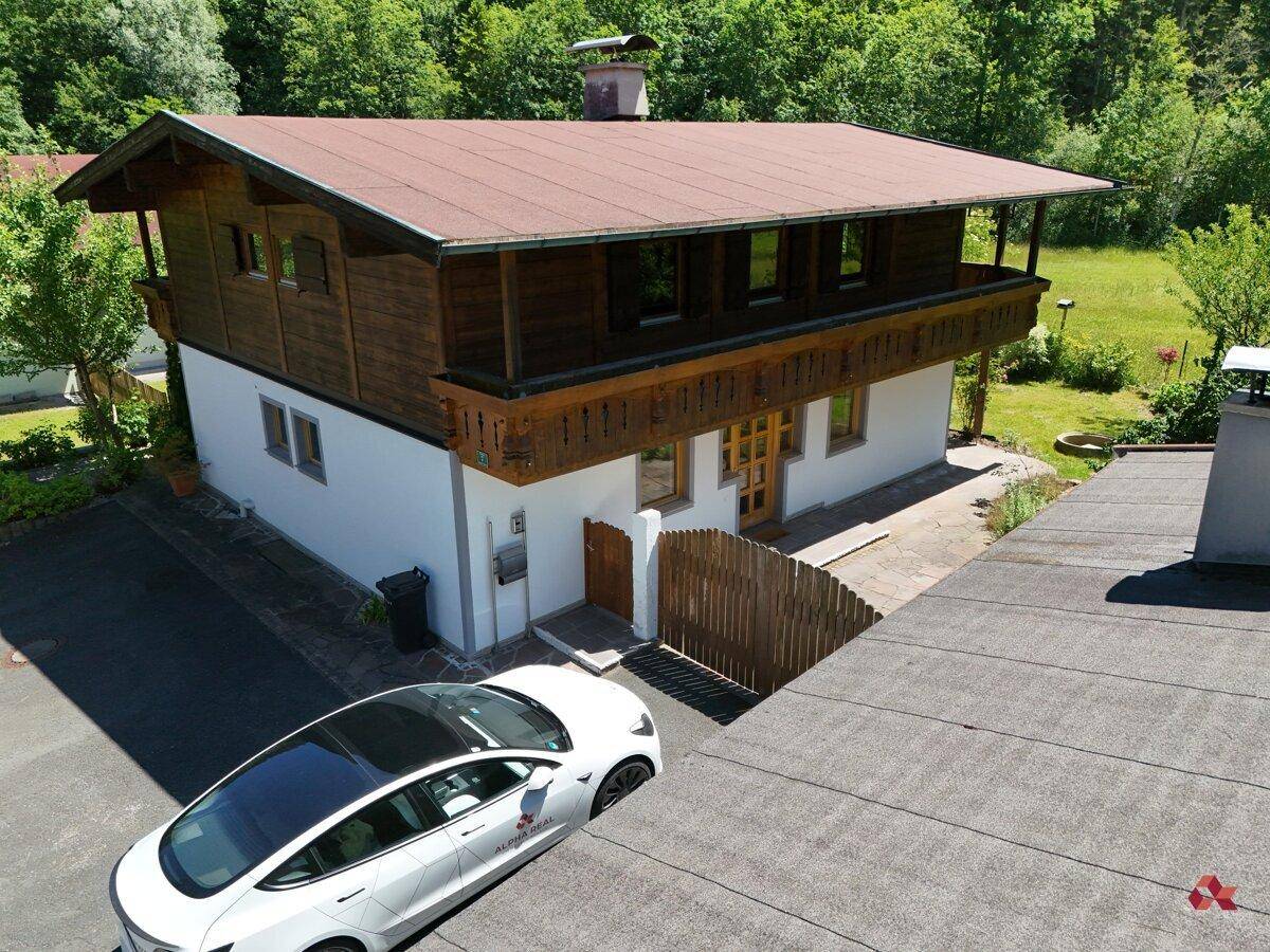 Traditionelles Holzhaus mit weißer Fassade, Holzbalkonen und einem modernen Elektroauto auf dem Parkplatz.
