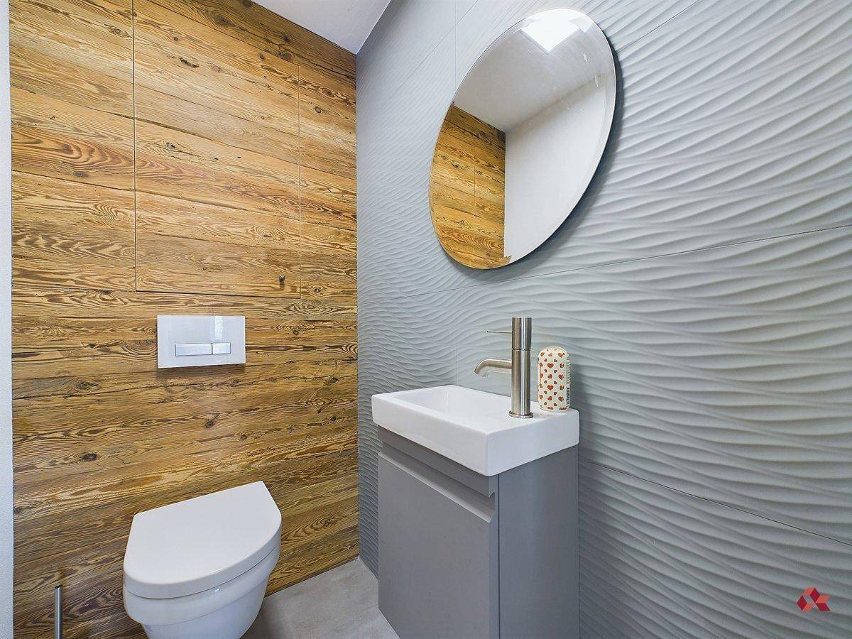 Modernes Gäste-WC mit Holzwandverkleidung, wellenförmigen Fliesen und stilvollem Waschbecken.