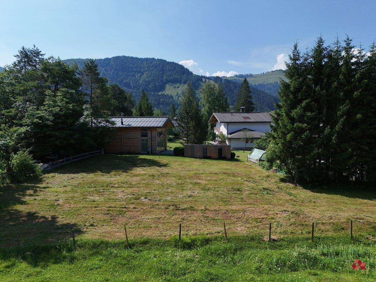 Idyllische Landschaft mit grünen Wiesen, Bäumen und Häusern vor einer Bergkulisse.