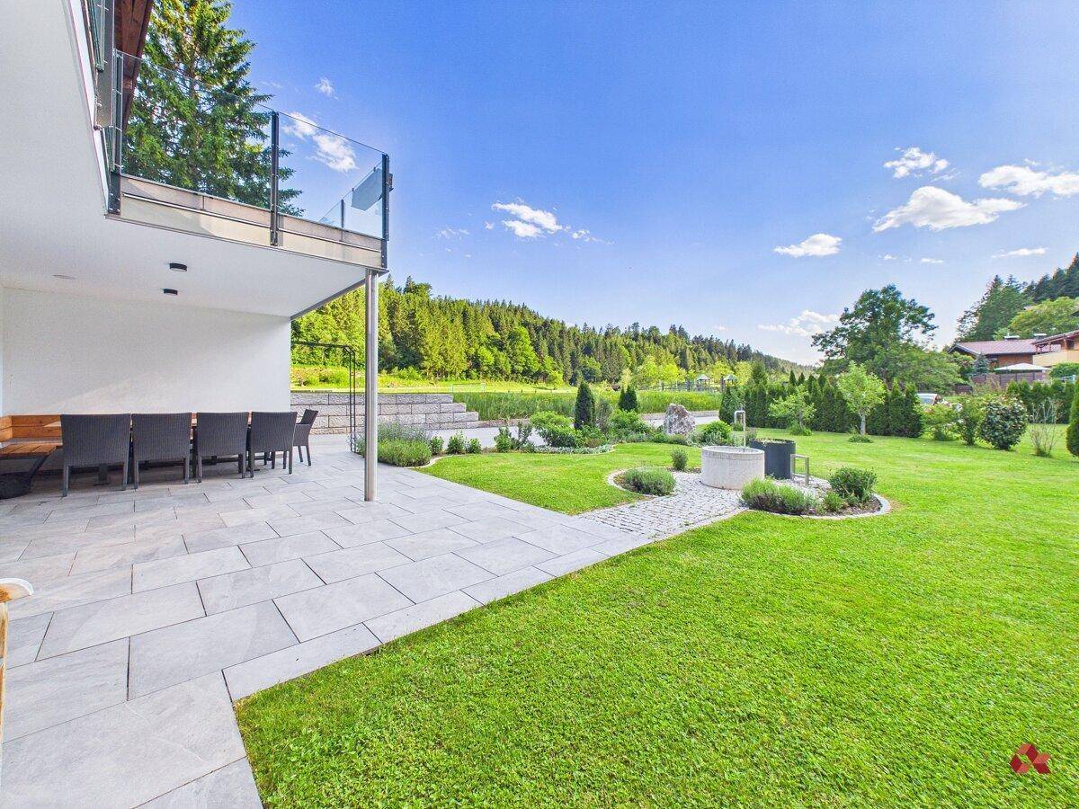 Gepflegter Garten mit Rasenfläche, Blumenbeeten und einer großzügigen Terrasse.