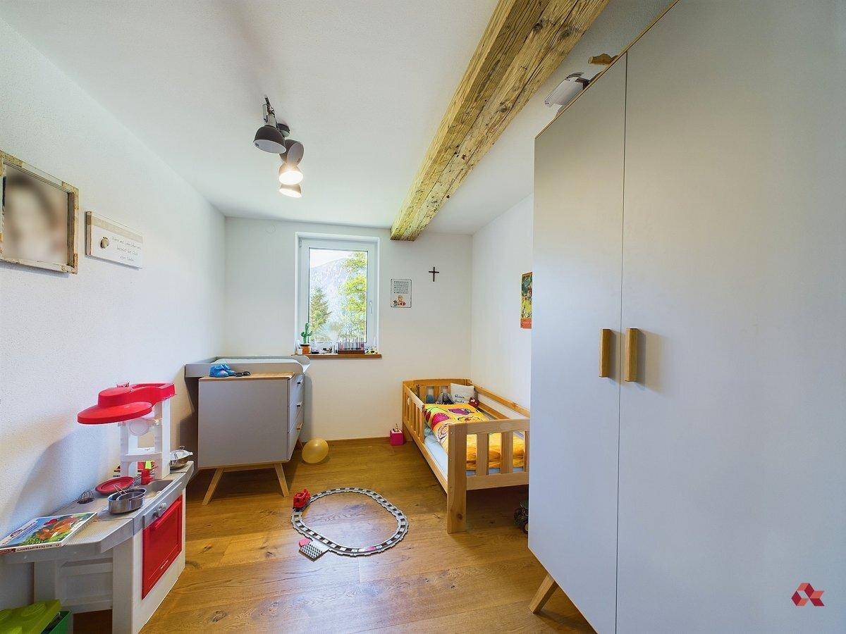 Helles Kinderzimmer mit Babybett, Wickeltisch, Kleiderschrank und sichtbarem Holzbalken.