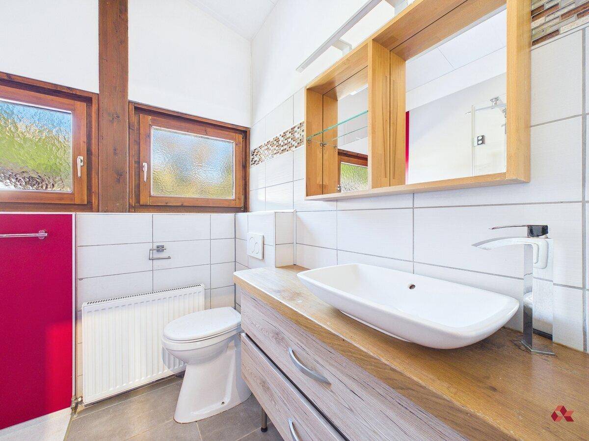 Badezimmer mit modernem Waschtisch, WC und Fenster, hell gefliest.