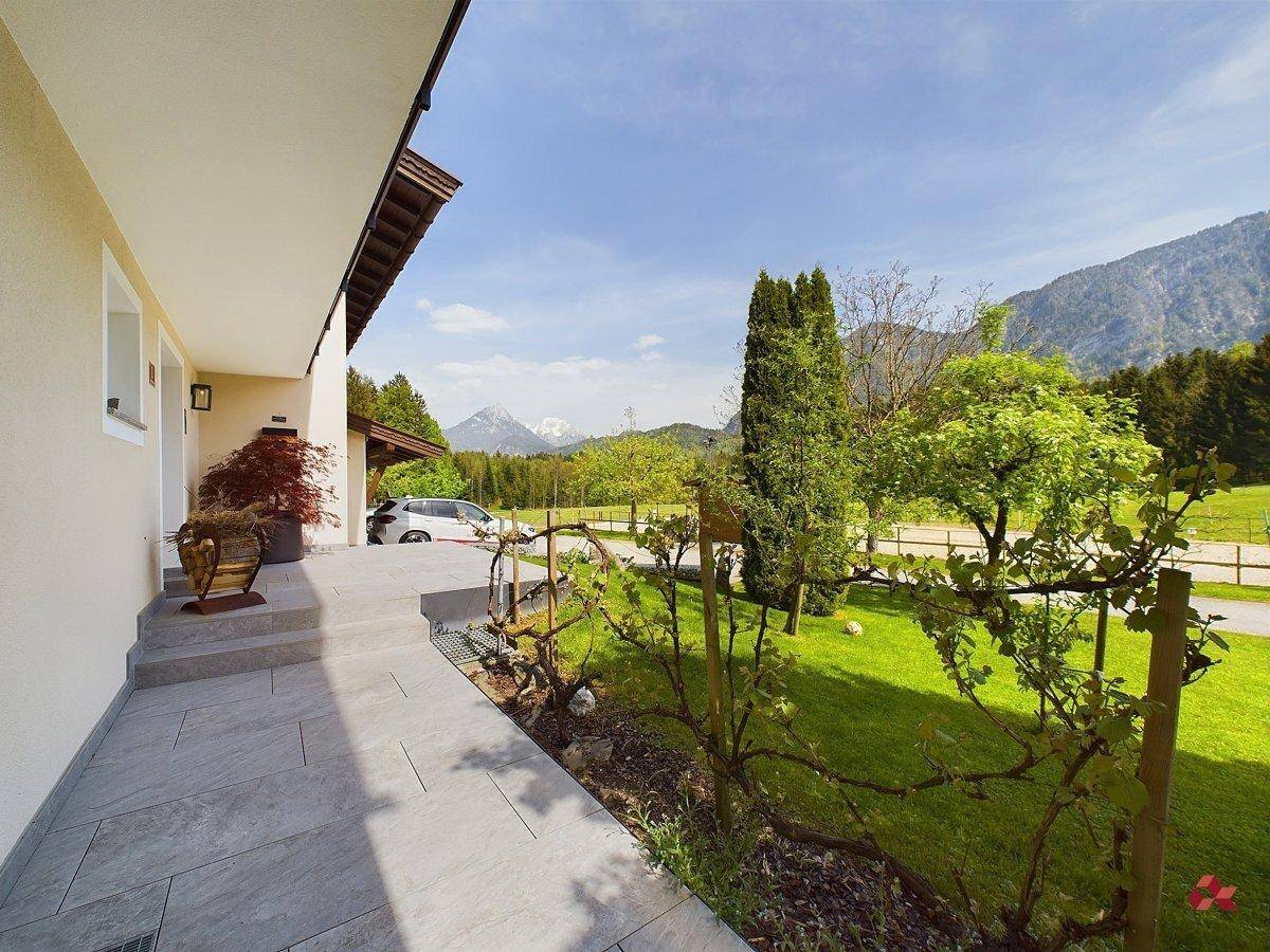 Seitenansicht des Hauses mit gepflegtem Rasen, gefliestem Weg und Bergblick in der Ferne.