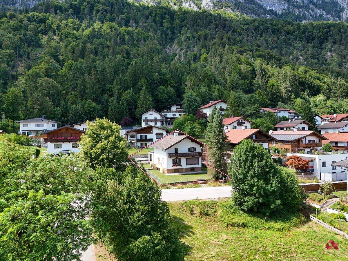 Luftaufnahme eines Hauses mit rotem Dach und umliegenden Häusern in einer grünen Berglandschaft.
