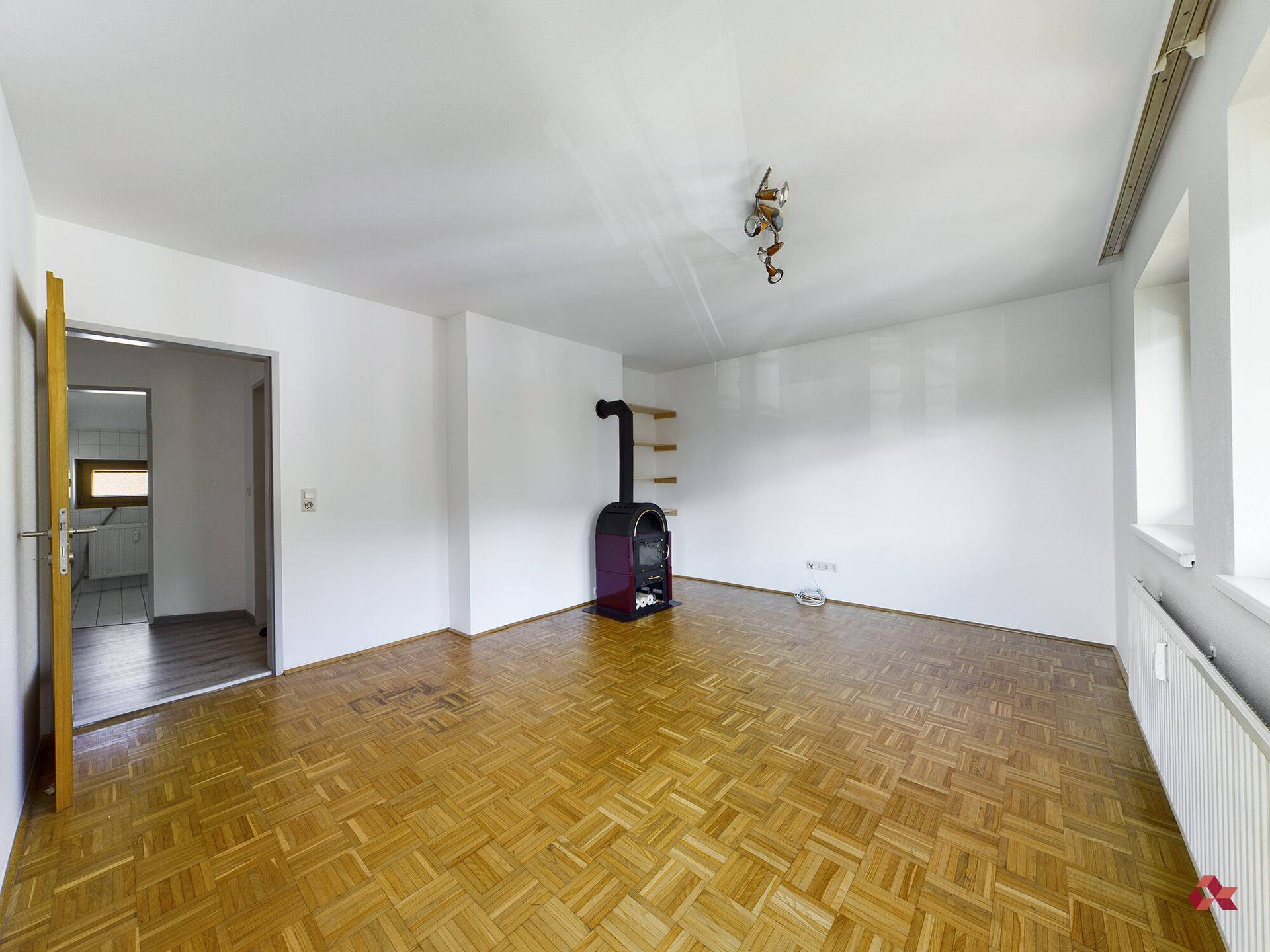Heller Raum mit Parkettboden und einem stilvollen Holzofen, bereit zur individuellen Gestaltung.