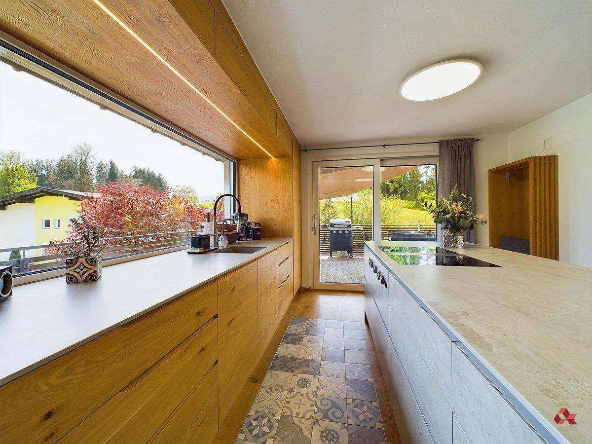 Moderne Holzküche mit gemusterten Fliesen, großem Fenster und Schiebetür zum Außenbereich.