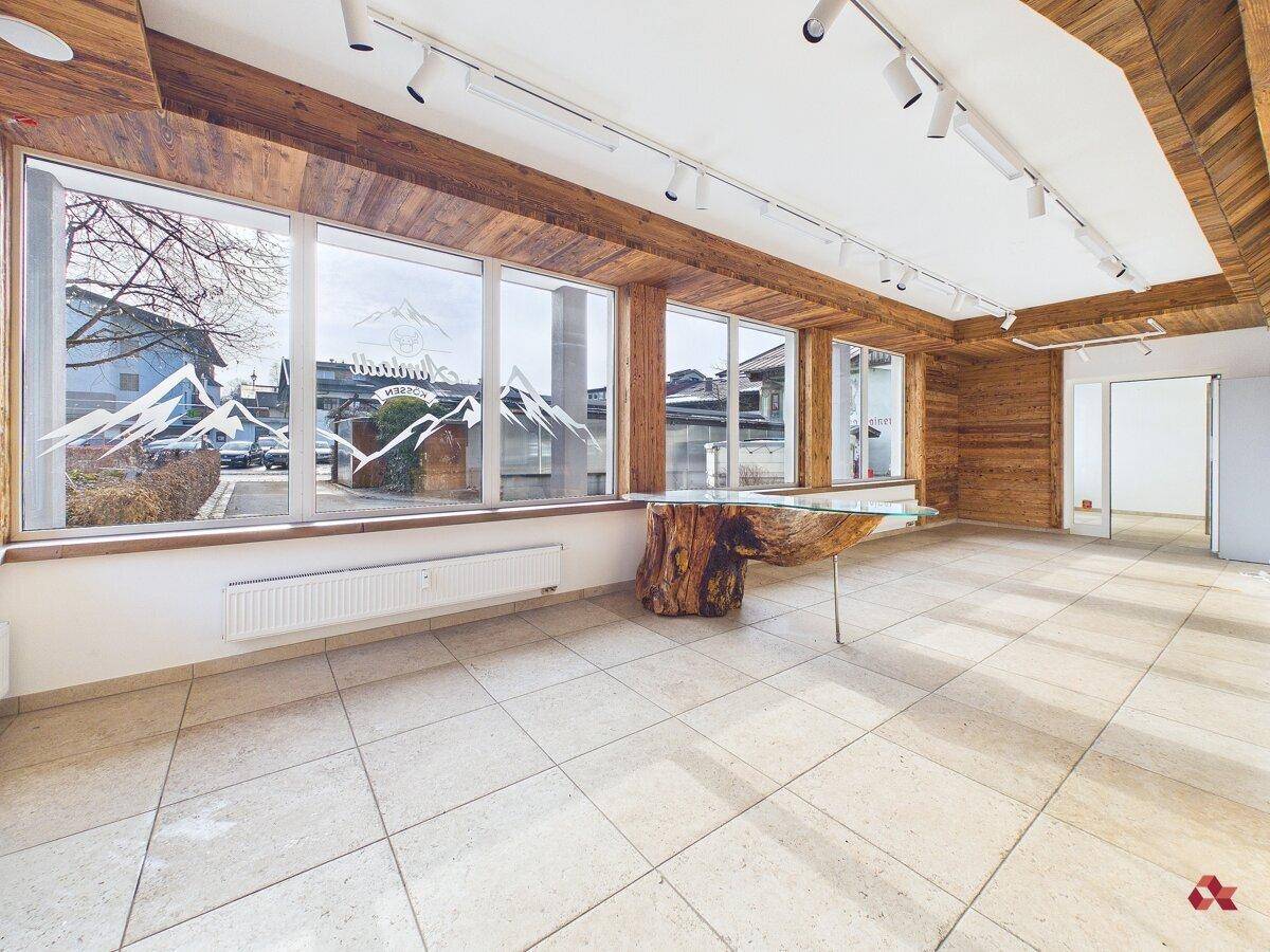 Großer, heller Raum mit Holzwänden und -decken, Fliesenboden und einer Fensterfront mit Blick nach draußen.