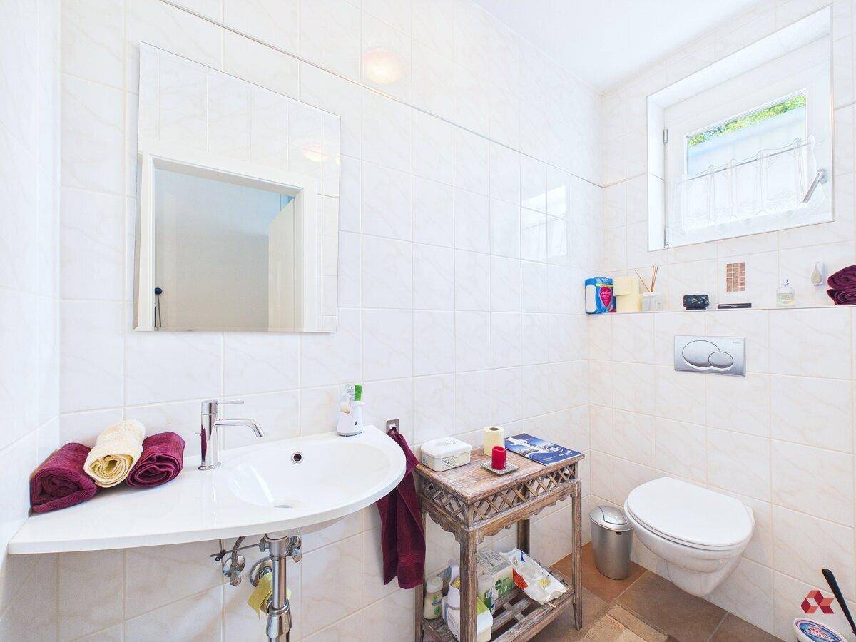 Helles Badezimmer mit weißen Fliesen, modernem Waschbecken, Toilette und Fenster für Tageslicht.