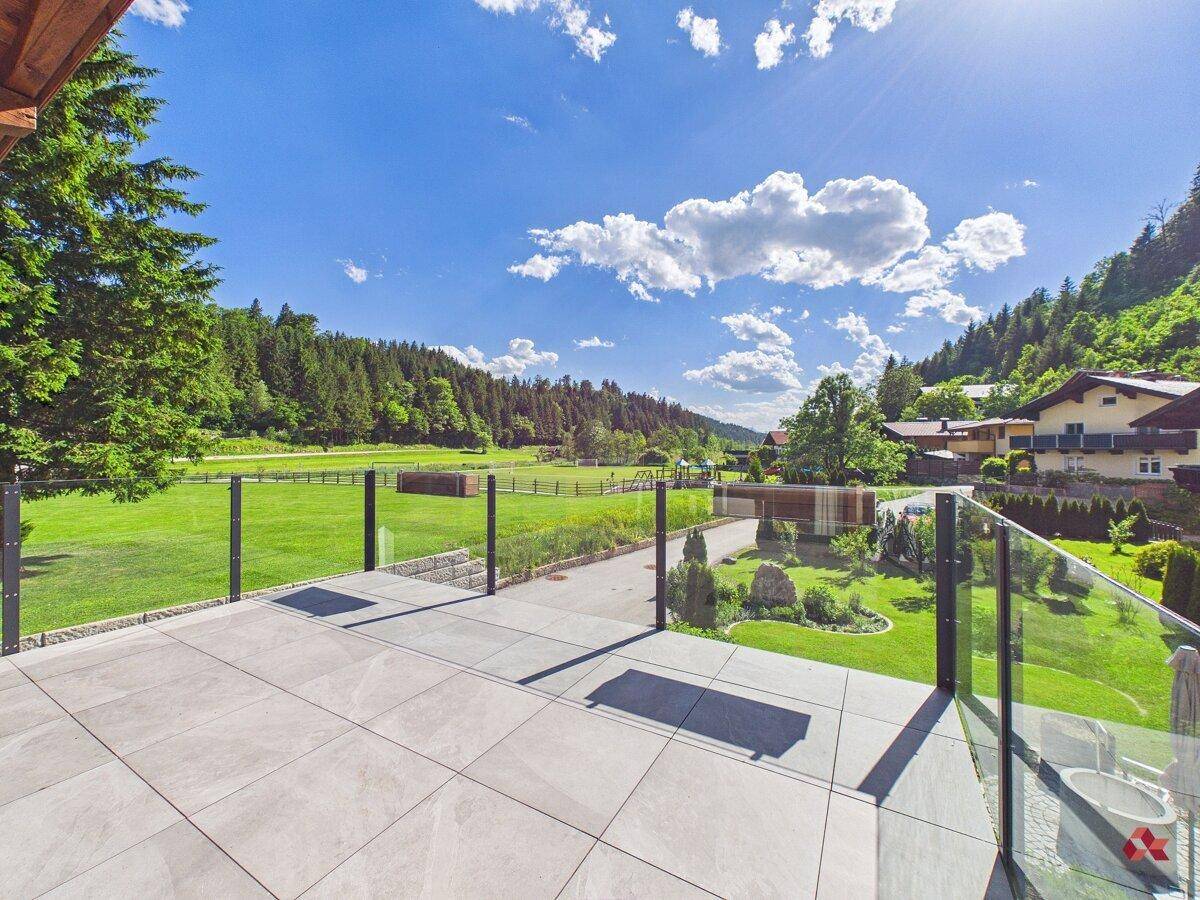 Große gepflasterte Terrasse mit Glasgeländer und weitem Blick ins Grüne.