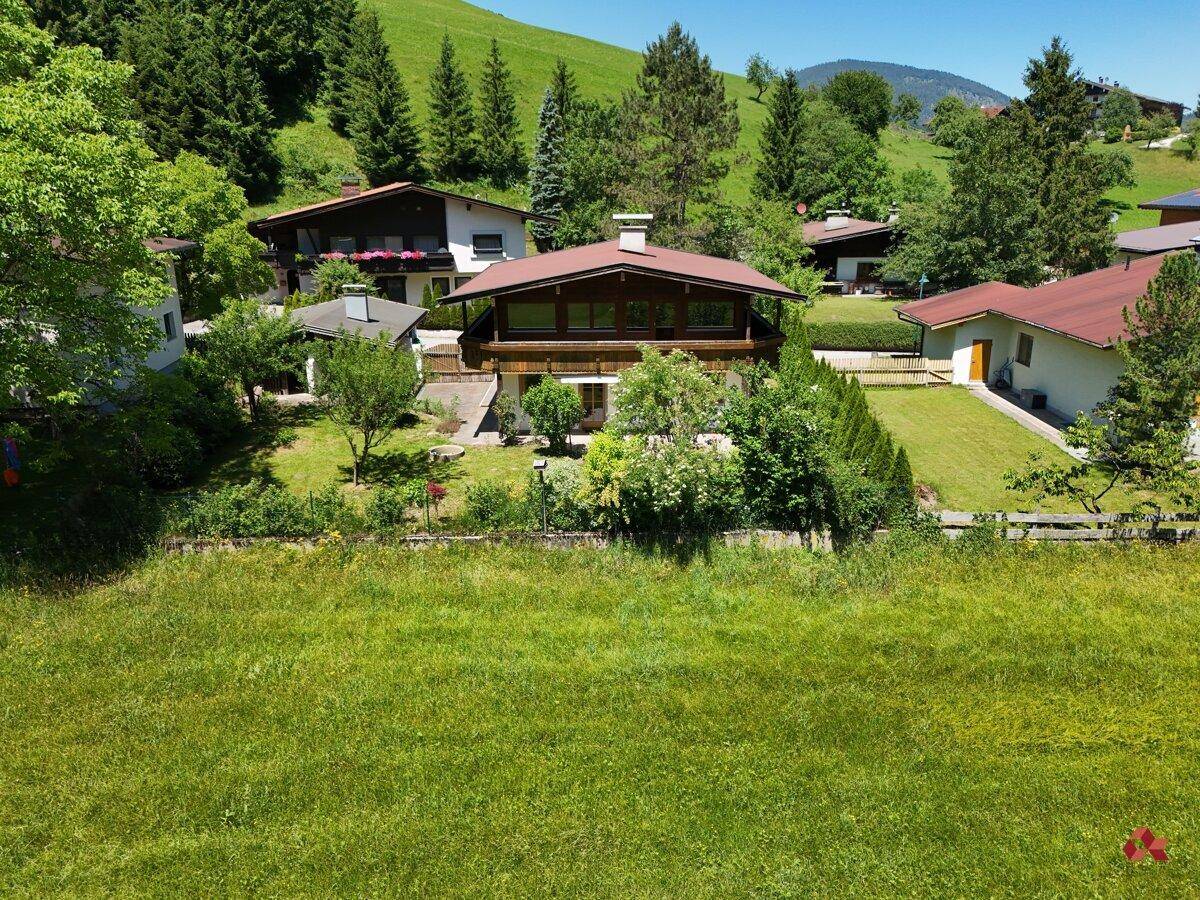Traditionelles Haus im alpinen Stil mit Satteldach, umgeben von grünen Wiesen und Bäumen in den Bergen.