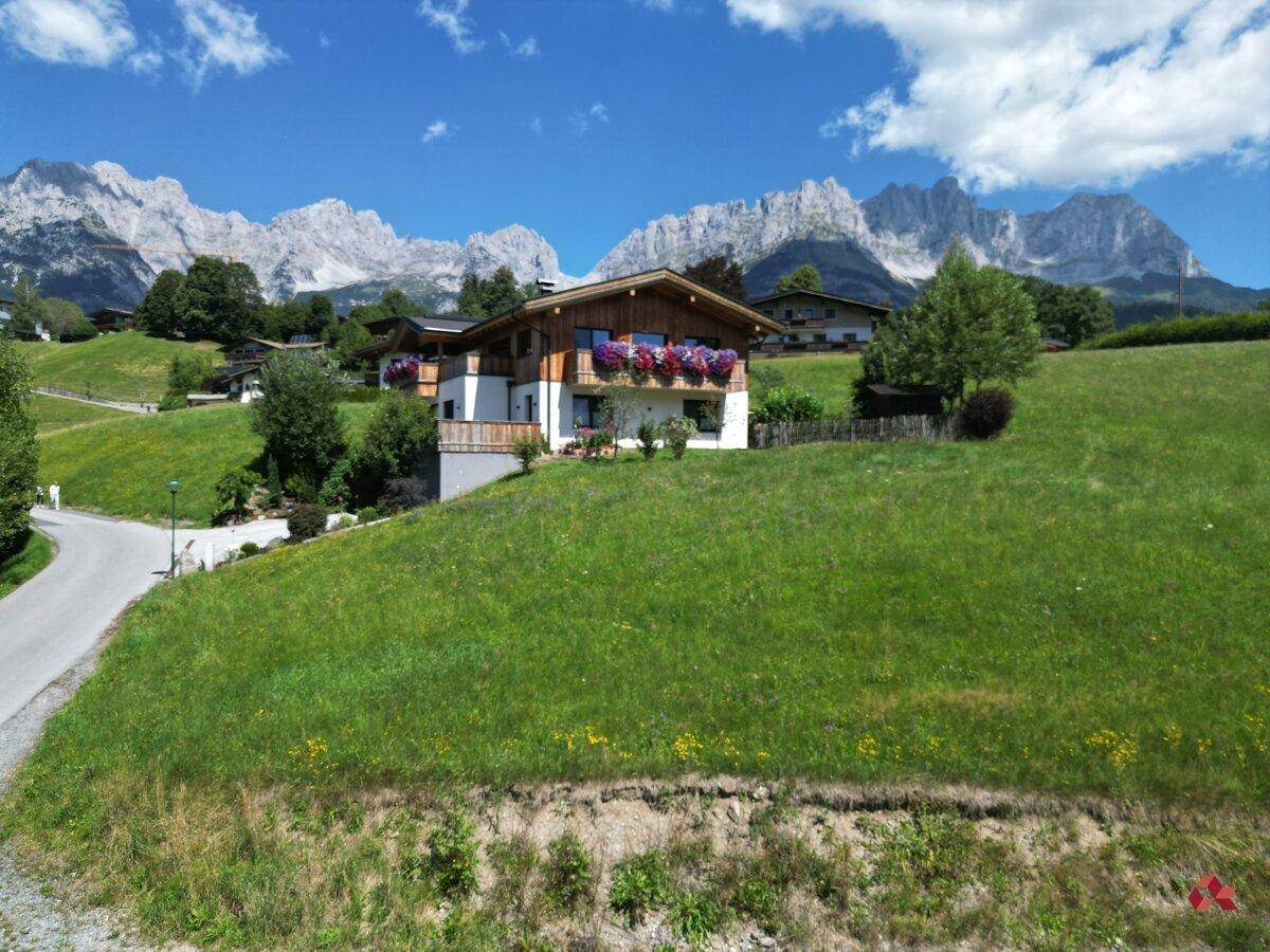 Idyllisches Haus mit blühenden Blumenkästen vor majestätischer Bergkulisse und grünen Wiesen.