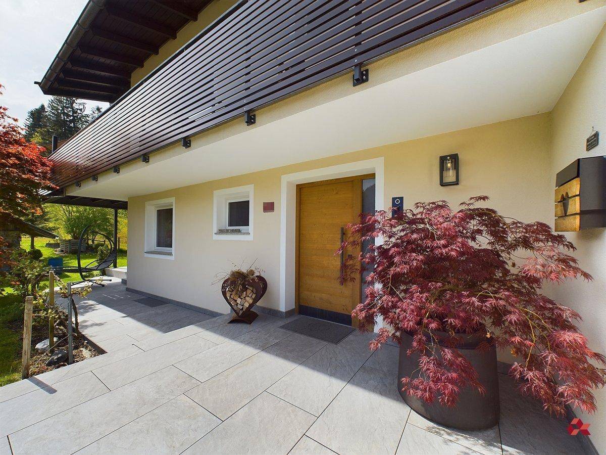 Einladender Eingangsbereich des Hauses mit gefliestem Weg, Holztür und dekorativen Pflanzen.