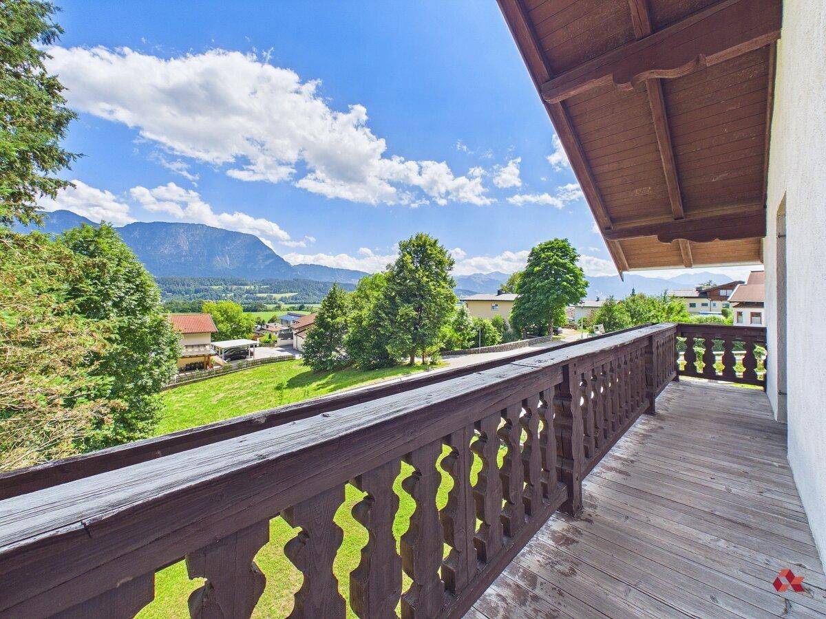 Traditioneller Holzbalkon mit geschnitztem Geländer und weitem Blick über die grüne Landschaft und Berge.