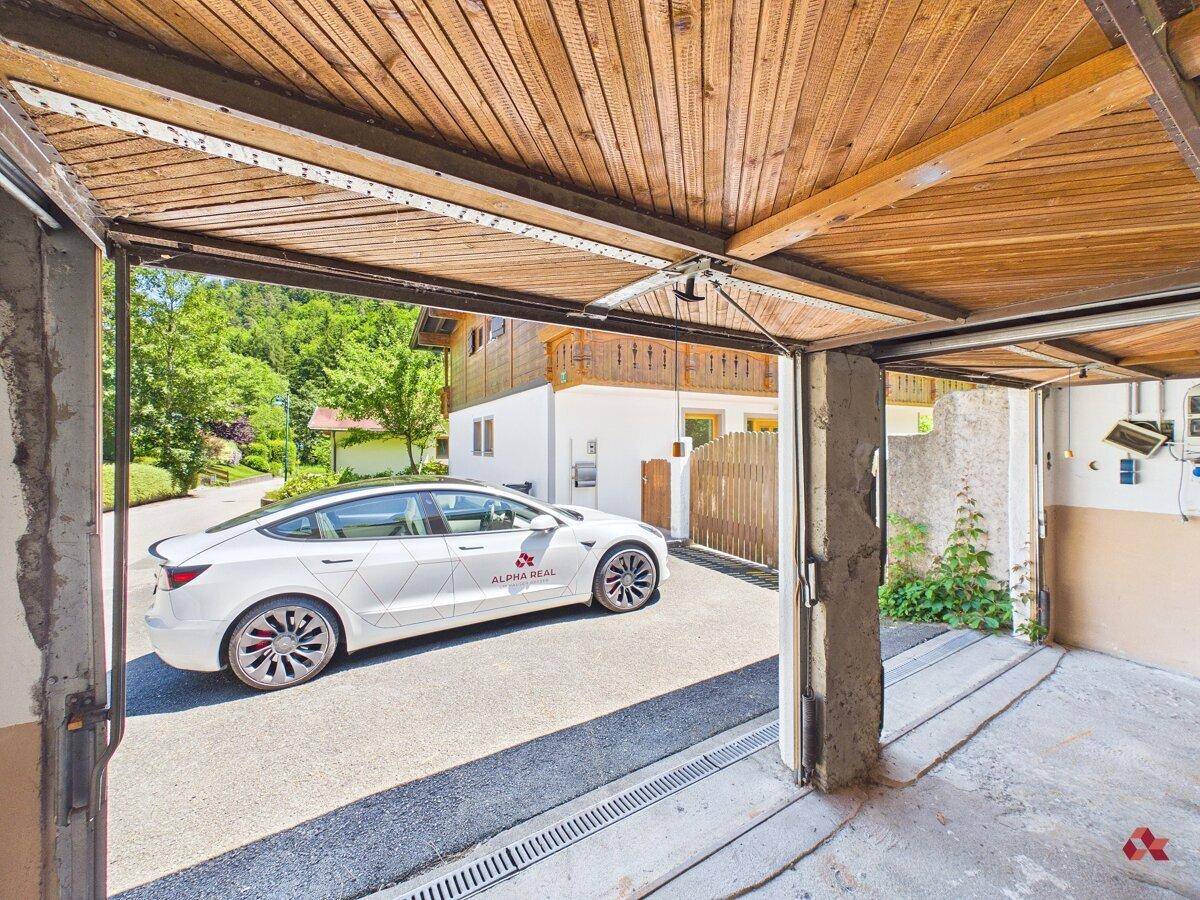 Helle Garage mit Holzbalken und Blick auf die Einfahrt mit einem Elektrofahrzeug.