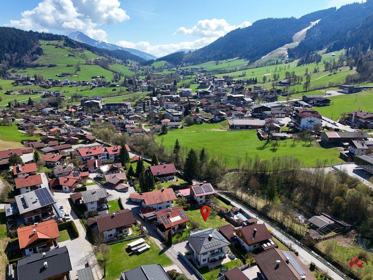 Ausgedehnte Luftaufnahme eines Bergdorfes mit weitem Blick über das Tal und die umliegenden Gipfel.