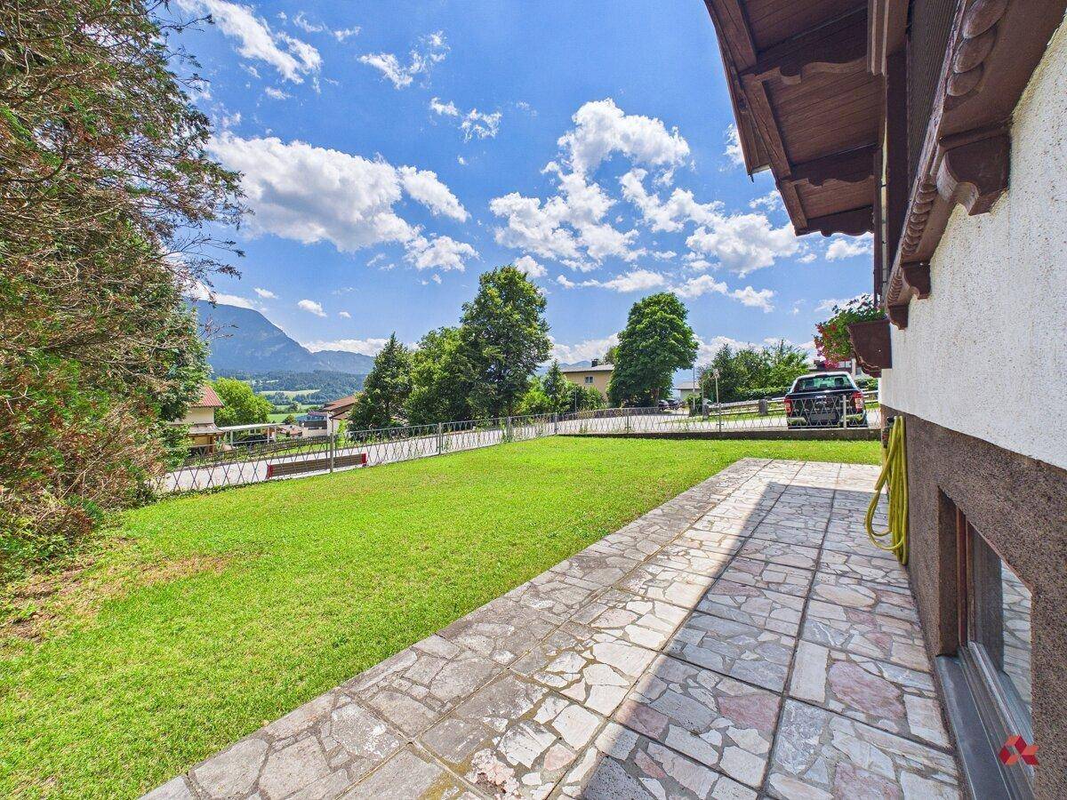 Gepflegter Rasen und eine Steinterrasse neben dem Haus mit Blick auf die umliegende Landschaft und Berge.