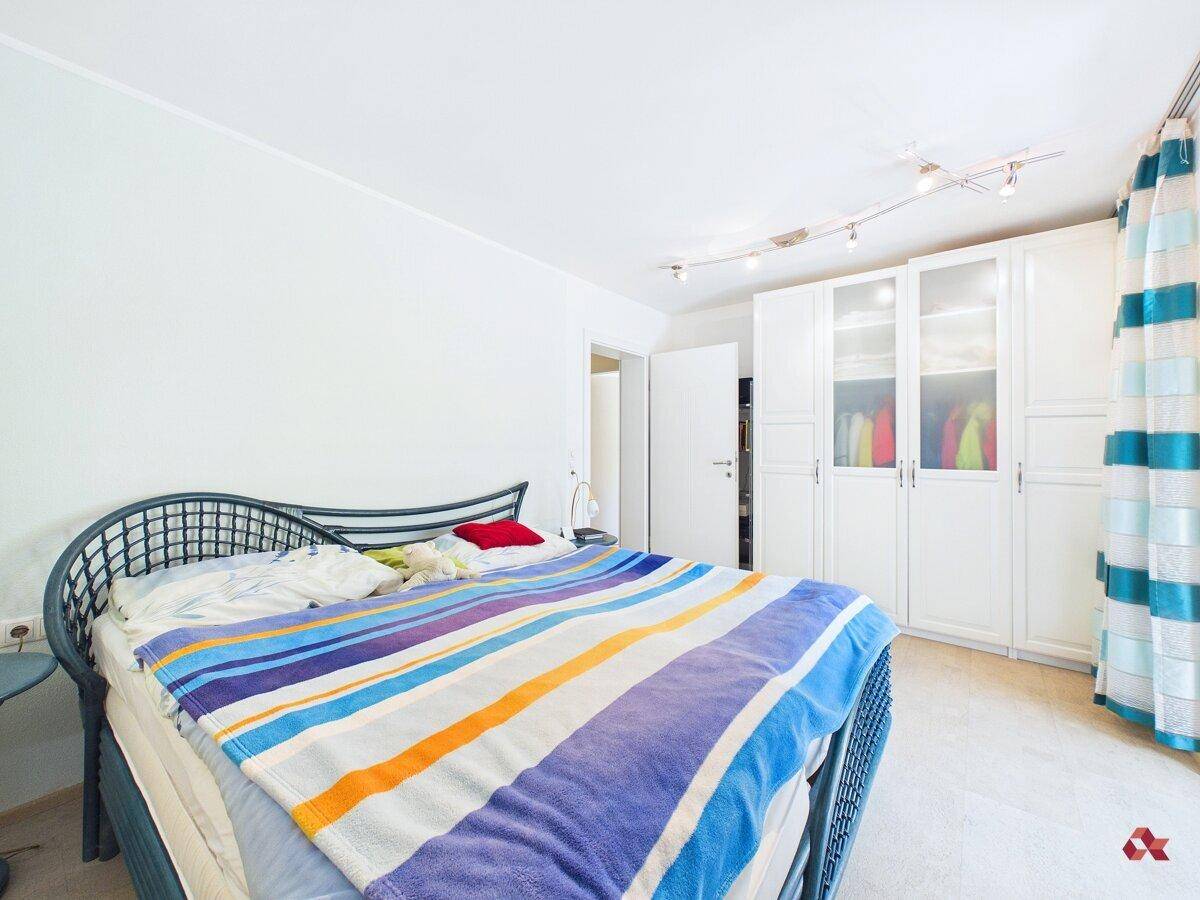 Helles Schlafzimmer mit Doppelbett, weißem Kleiderschrank und moderner Beleuchtung.