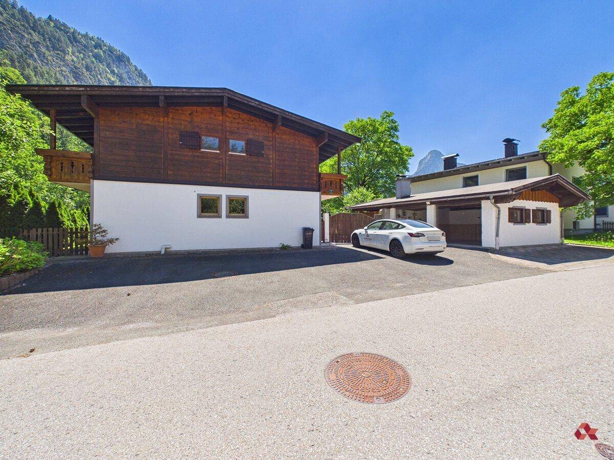 Traditionelles Haus mit Carport und gepflegter Einfahrt, umgeben von üppiger Natur.