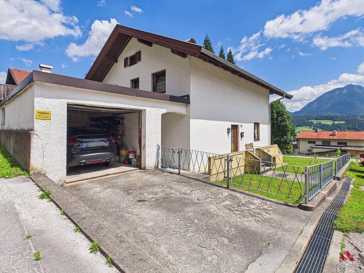 Vorderansicht des Hauses mit integrierter Garage, Einfahrt und einem kleinen umzäunten Vorgarten.