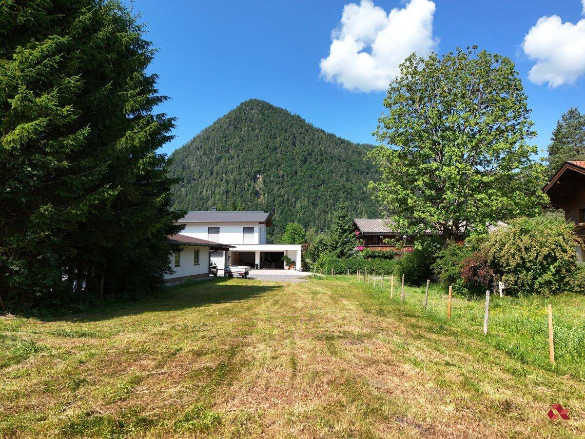 Offene Wiesenfläche mit Blick auf bewaldete Berge und umliegende Wohnhäuser.