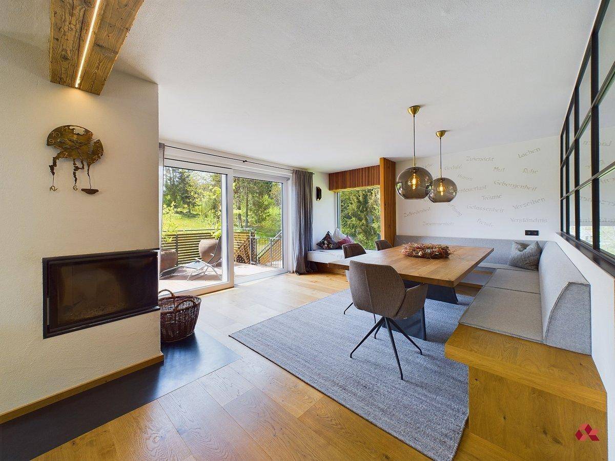 Offener Wohn- und Essbereich mit Kamin, Holzboden und Zugang zu einer sonnigen Terrasse.