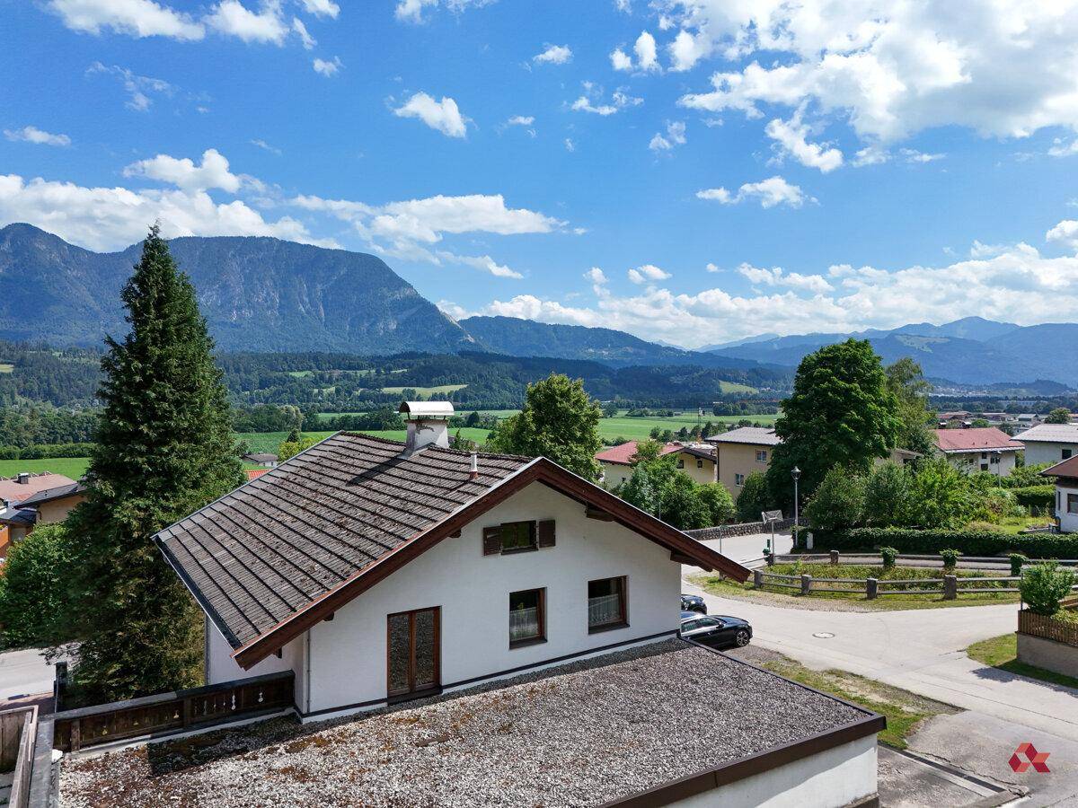 Panoramablick über das Hausdach auf eine weite grüne Landschaft mit majestätischen Bergen im Hintergrund.