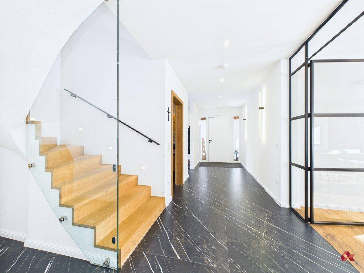 Heller Flur mit moderner Holztreppe, Glasgeländer und dunklem Fliesenboden.