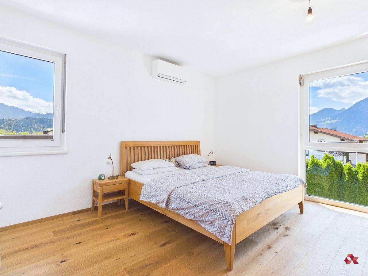 Schlafzimmer mit Holzbett, Parkettboden, Klimaanlage und Bergblick aus dem Fenster.