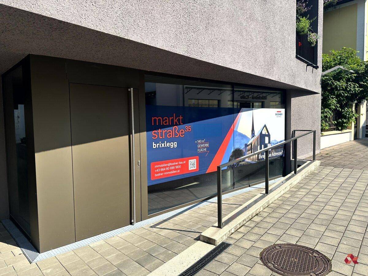 Eingangsbereich eines modernen Geschäftsgebäudes mit großer Glasfront und Werbebanner für Gewerbeflächen.