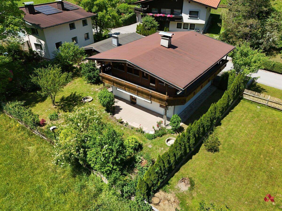 Luftaufnahme eines Hauses im alpinen Stil mit Terrasse und gepflegtem Gartenbereich, umgeben von Hecken.