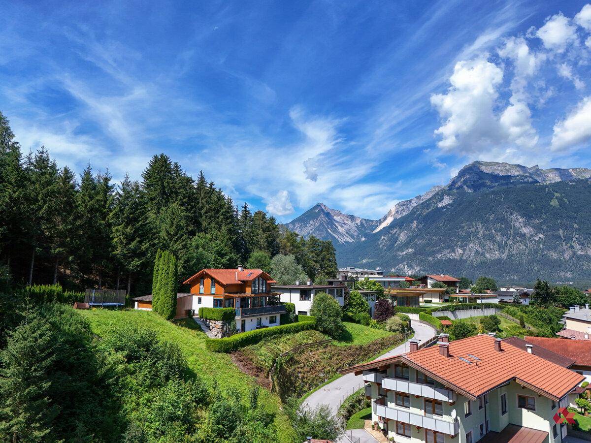 Weitläufiger Blick über eine Siedlung mit Häusern und üppiger Vegetation vor einer beeindruckenden Bergkulisse.
