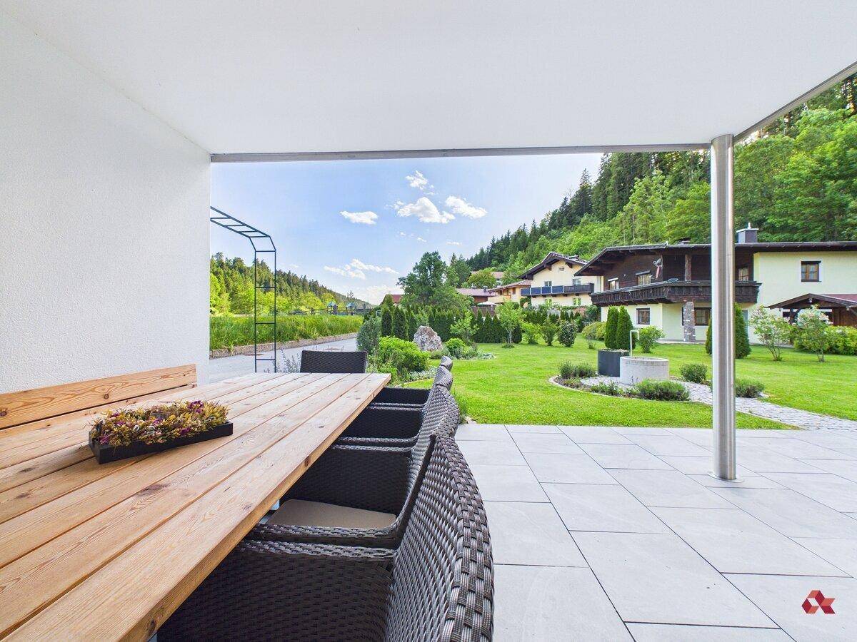 Überdachte Terrasse mit Holztisch und Rattanmöbeln, umgeben von viel Grün.