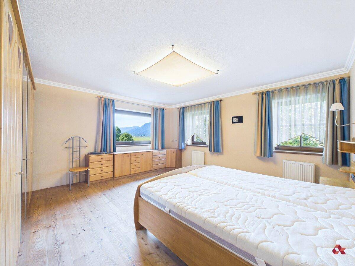 Schlafzimmer mit Doppelbett, Holzschränken und Fenstern mit weitem Blick auf die Landschaft.