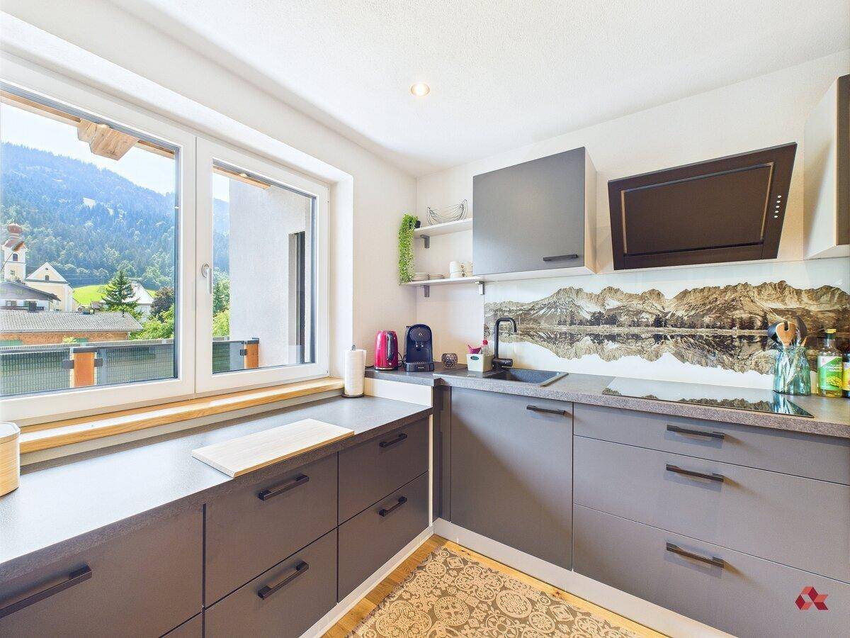 Moderne Küche mit Fenster und Bergblick, ausgestattet mit grauen Schränken und Kochfeld.