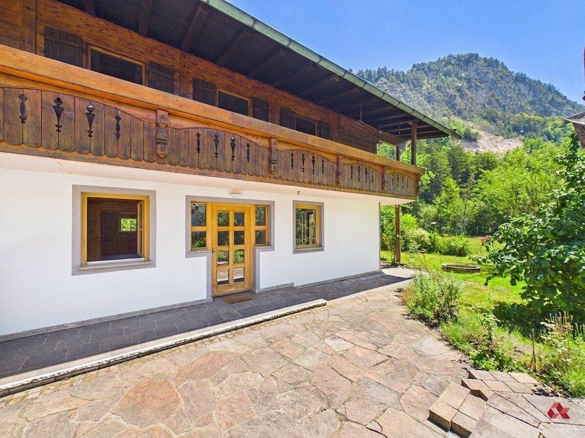 Rustikale Steinterrasse vor dem Haus mit Holzelementen und Blick ins Grüne.