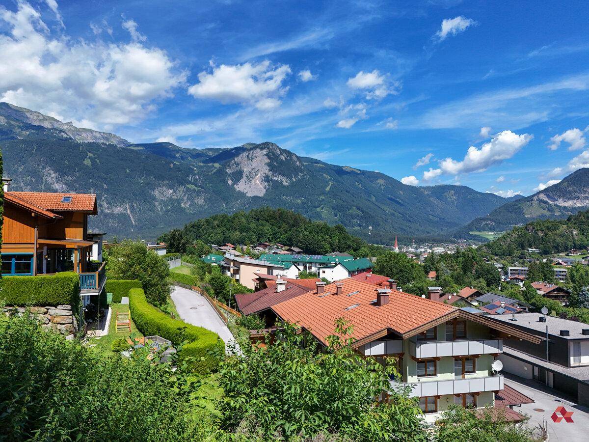 Malerische Ansicht einer Wohnsiedlung in den Bergen, mit traditionellen Häusern und grünen Hängen unter strahlend blauem Himmel.