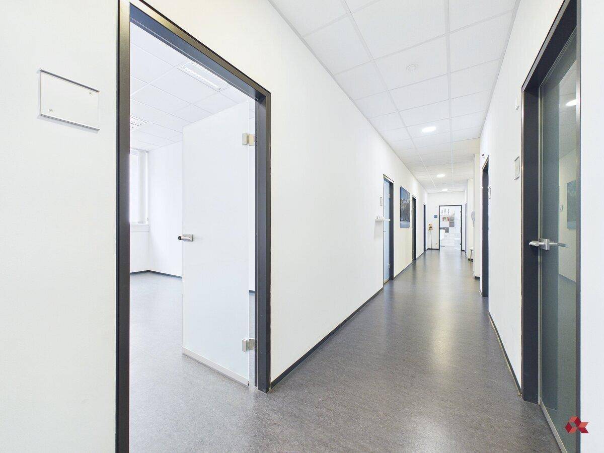 Langer, heller Flur mit mehreren Bürotüren und grauem Bodenbelag, der zu den einzelnen Räumen führt.
