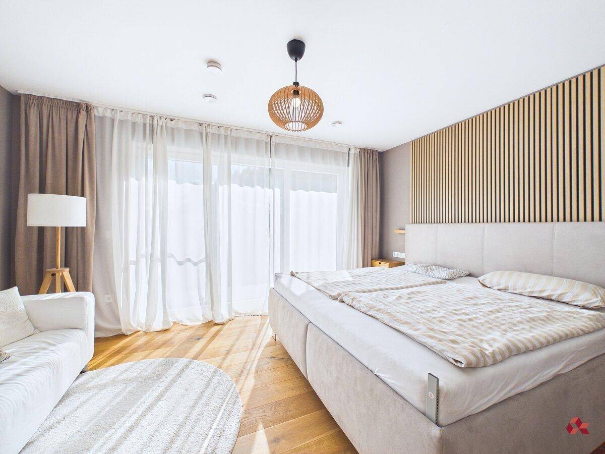 Helles Schlafzimmer mit Doppelbett, Holzboden und Zugang zum Balkon.