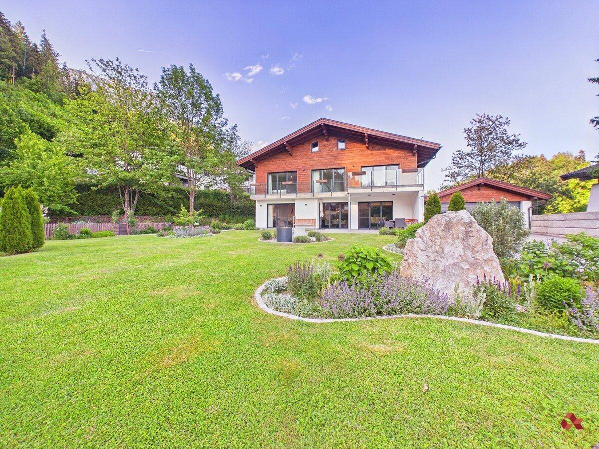 Großzügiger Garten mit Rasenflächen, Zierpflanzen und einem modernen Wohnhaus im Hintergrund.