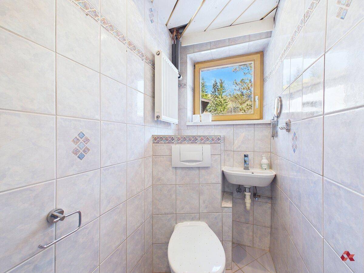 Kleines Gäste-WC mit Fenster, Wand-WC und Waschbecken, hell gefliest.