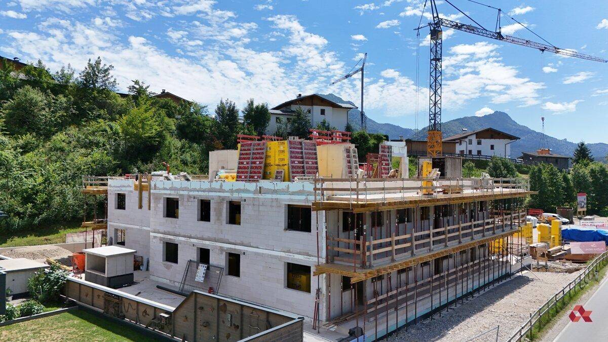 Baustelle eines Mehrfamilienhauses im Rohbau mit Gerüst und Blick auf die umliegende Bebauung.