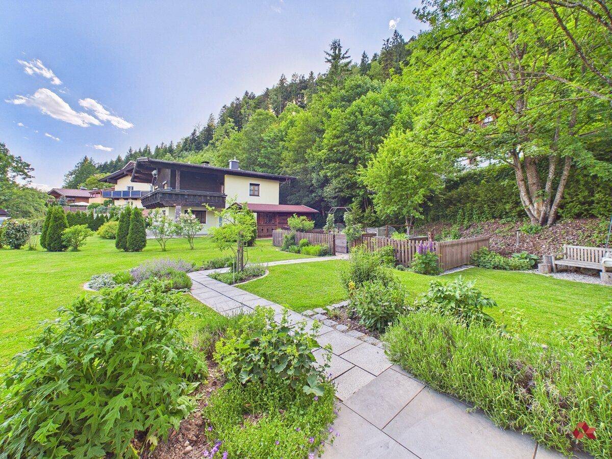 Idyllischer Gartenweg umgeben von üppigem Grün und Bäumen, mit Blick auf ein weiteres Haus.