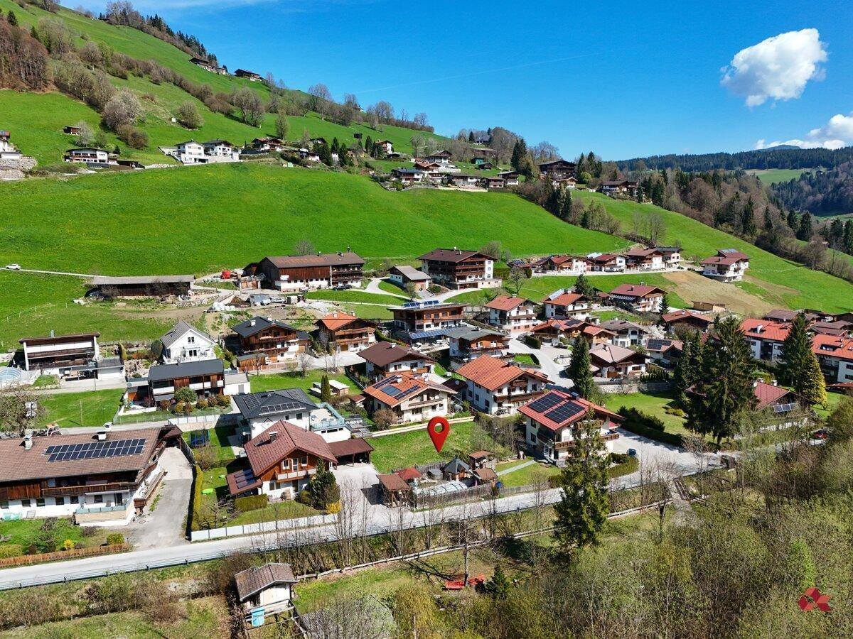 Weitläufige Luftaufnahme eines Dorfes in einem Tal, umgeben von grünen Hügeln und Bergen.